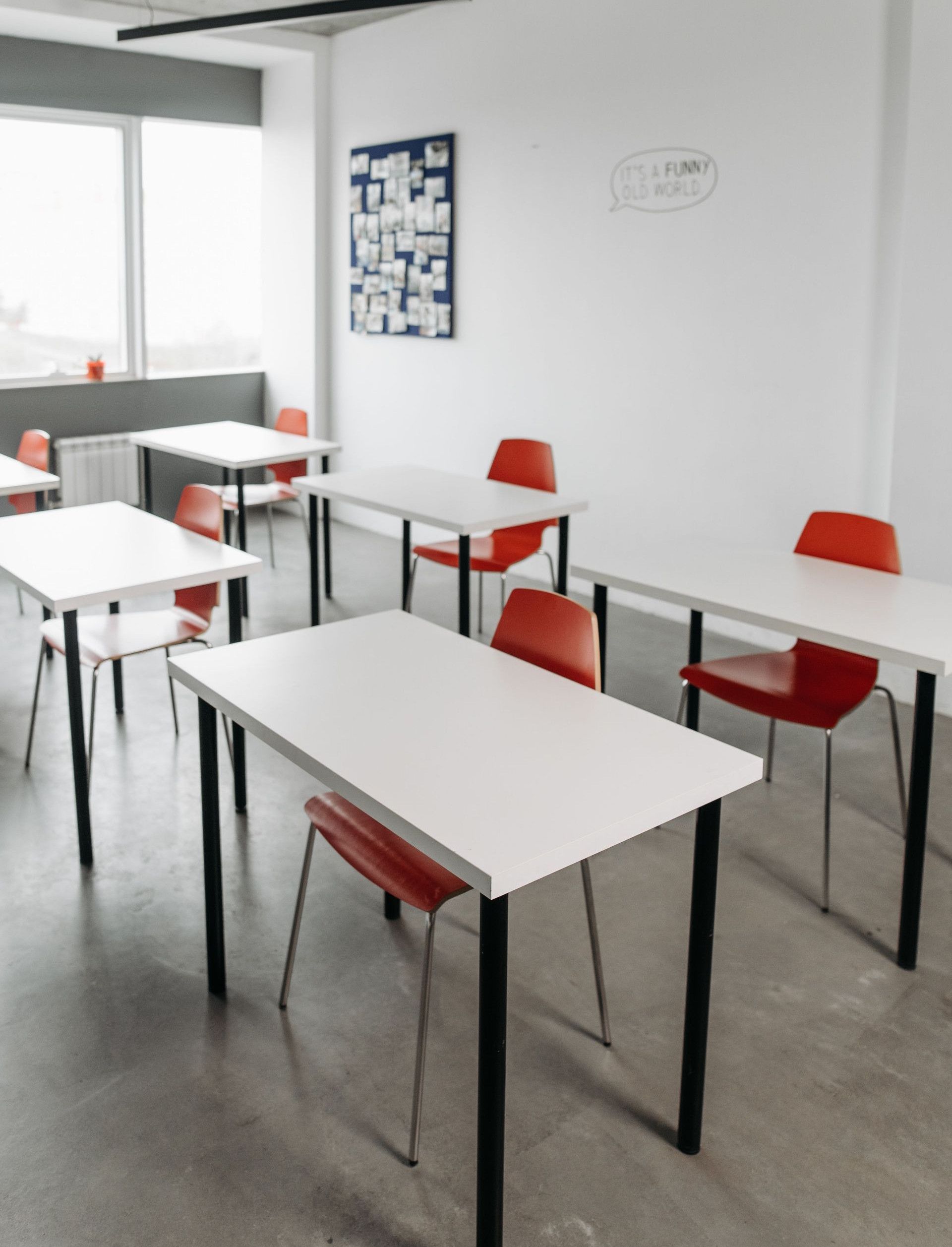 Contemporary classroom interior with red chairs and white desks arranged in rows.